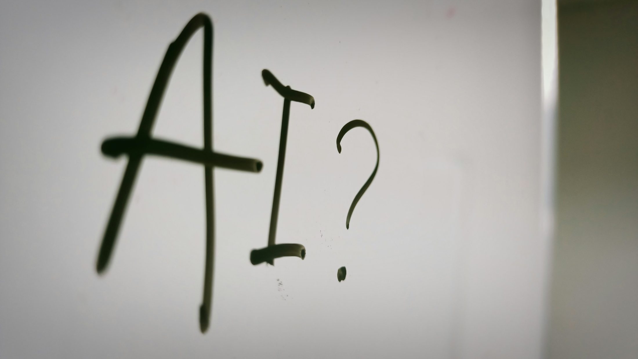The letters AI followed by a question mark, written in black marker on a whiteboard