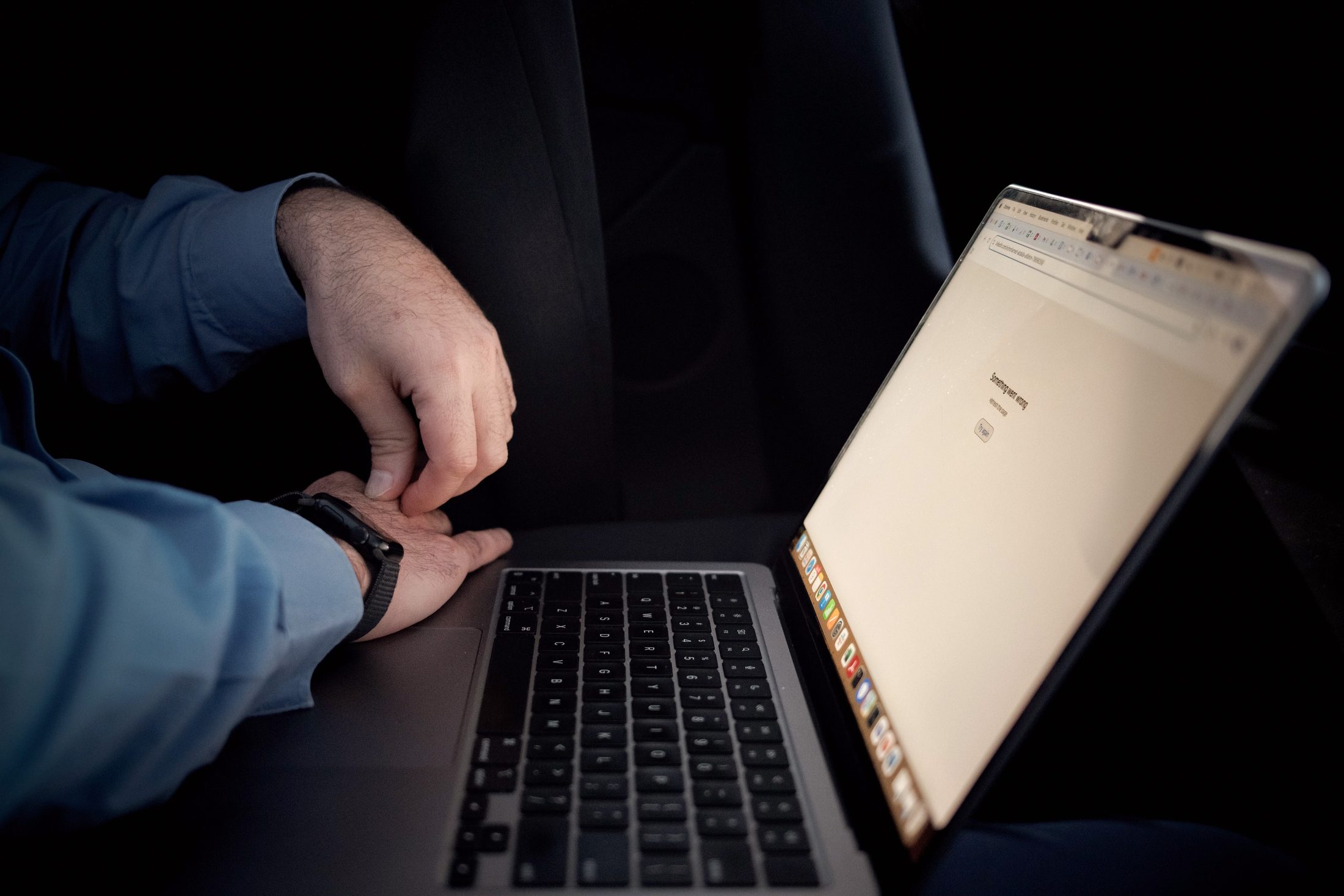 Two hands beside an open laptop in the dark, the screen showing an error page that reads Something went wrong